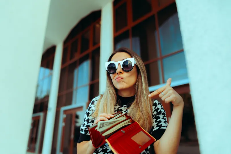 girl wearing glasses pointing at her wallet with money in it.