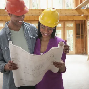 Happy couple wearing hard hats looking a home blueprint.